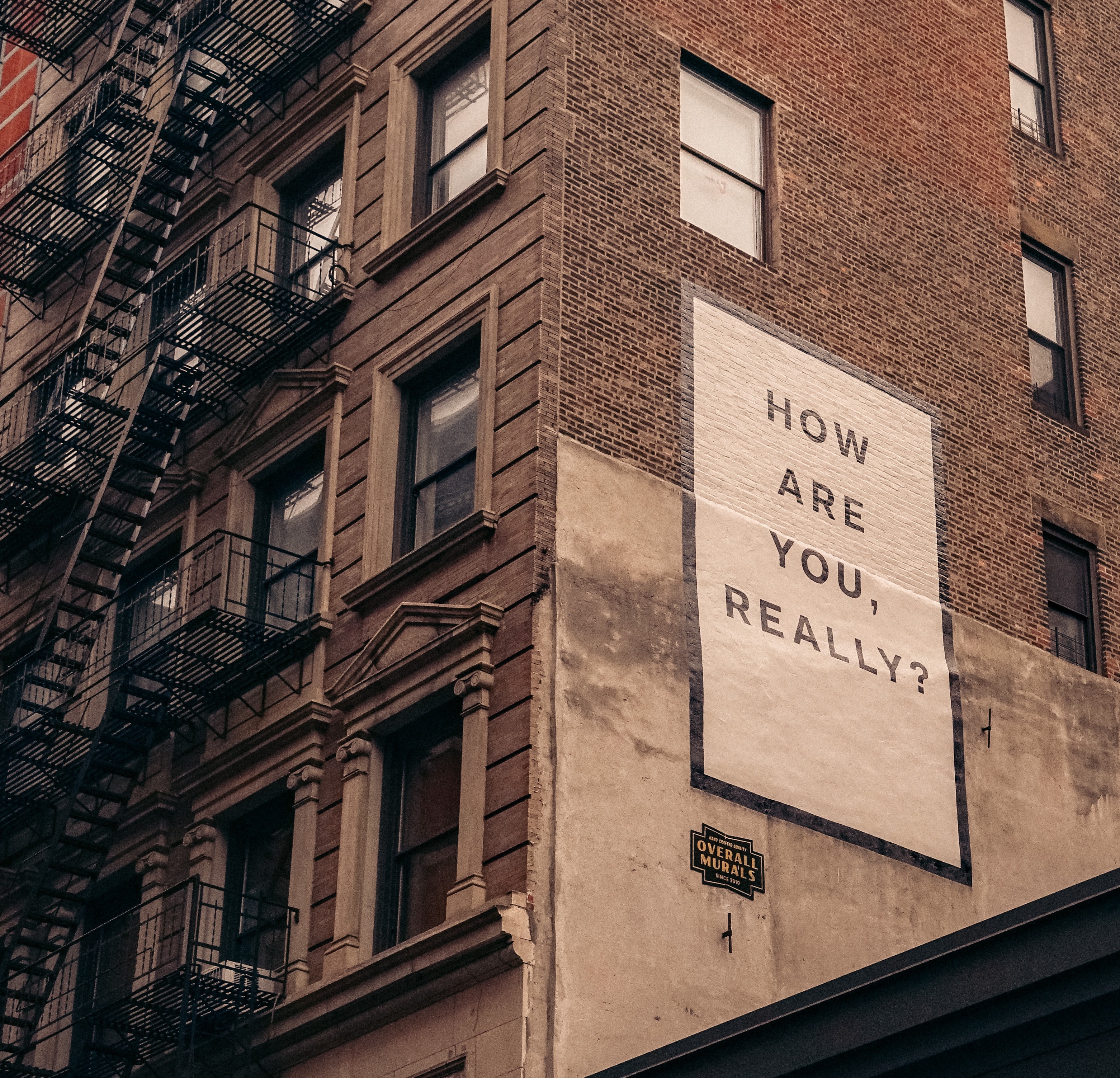 Photo of a brick building with the sign 'How are you really?"